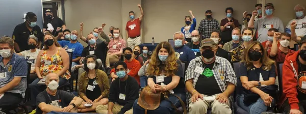 A room packed with attendees at the "New Trends in Revitalized Labor Councils" workshop at the 2022 Labor Notes Conference. Attendees, many of whom are wearing masks, are posing for a group photo. Some are cheering. Some have raised fists.